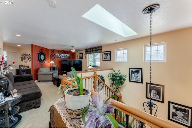 carpeted living room with ceiling fan, a textured ceiling, and a skylight