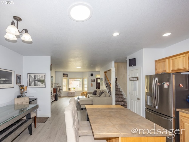 kitchen with stainless steel refrigerator with ice dispenser, a notable chandelier, tile countertops, decorative light fixtures, and light wood-type flooring