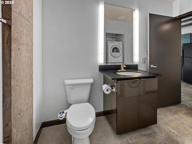 half bathroom featuring stacked washer / dryer, baseboards, vanity, and toilet