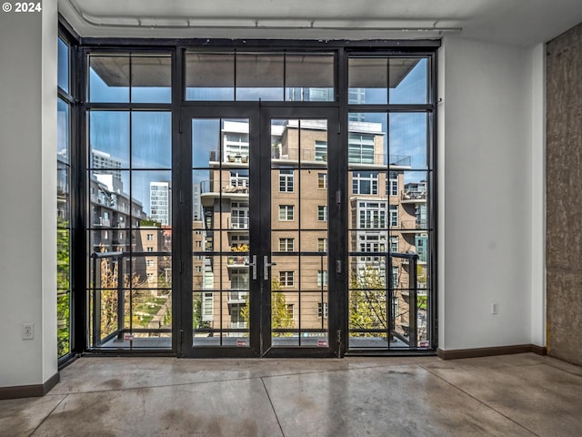 doorway to outside with concrete flooring, a view of city, baseboards, and a wall of windows