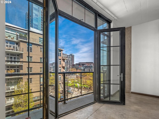 doorway to outside with a view of city, a wall of windows, baseboards, and concrete flooring