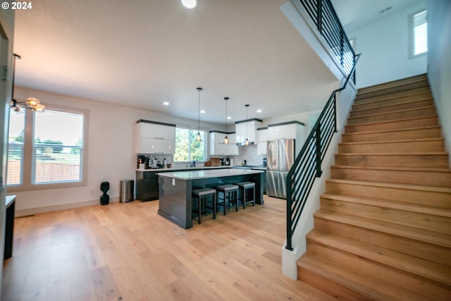 kitchen featuring stainless steel refrigerator, light wood-type flooring, a kitchen island, decorative light fixtures, and white cabinets