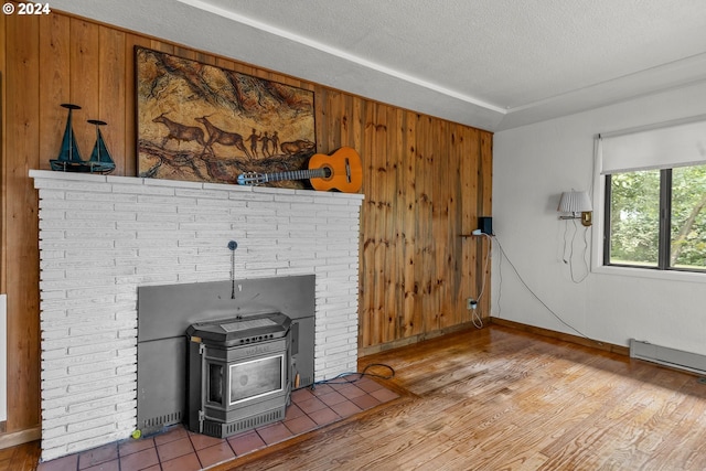 unfurnished living room featuring wood walls, a textured ceiling, hardwood / wood-style floors, and a wood stove