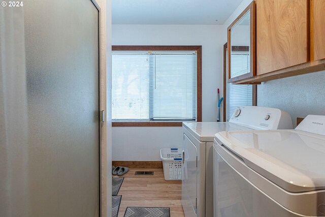 clothes washing area featuring cabinets, washing machine and clothes dryer, and light hardwood / wood-style floors