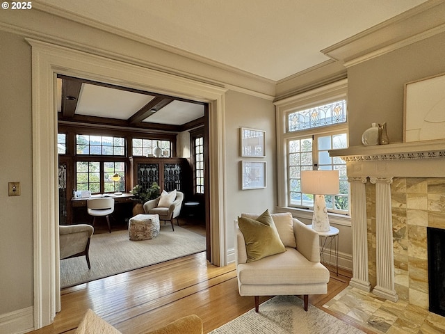 living area with beam ceiling, crown molding, light wood-type flooring, and a fireplace