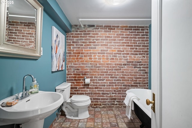 bathroom with brick wall, sink, a bathtub, and toilet