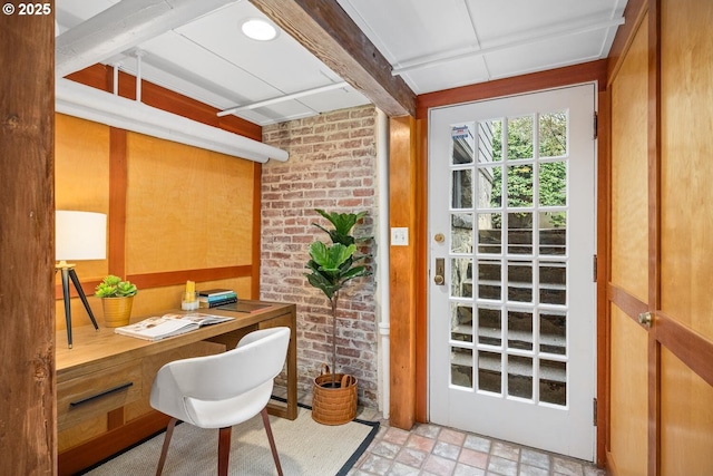 office with built in desk, beamed ceiling, and brick wall