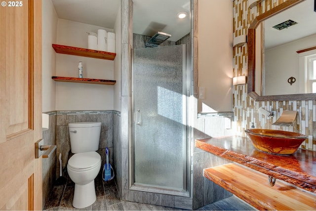 bathroom with toilet, an enclosed shower, sink, and tile walls