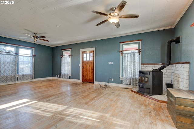 unfurnished living room with light wood-type flooring, ornamental molding, ceiling fan, and a wood stove