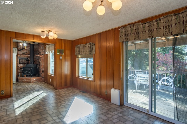 unfurnished dining area with wooden walls, a wood stove, and a textured ceiling