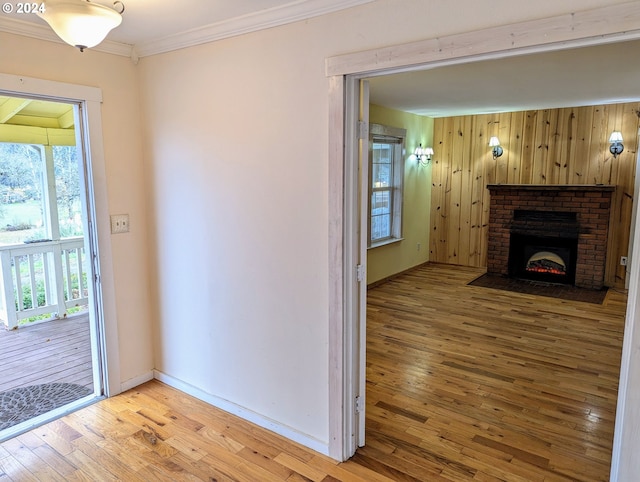 interior space with wooden walls, light hardwood / wood-style flooring, a brick fireplace, and ornamental molding