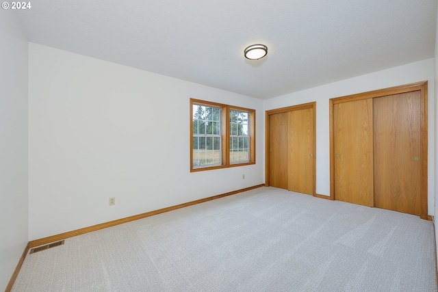 unfurnished bedroom with light carpet and two closets