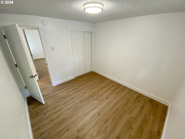 unfurnished bedroom featuring a closet, a textured ceiling, and light wood-type flooring