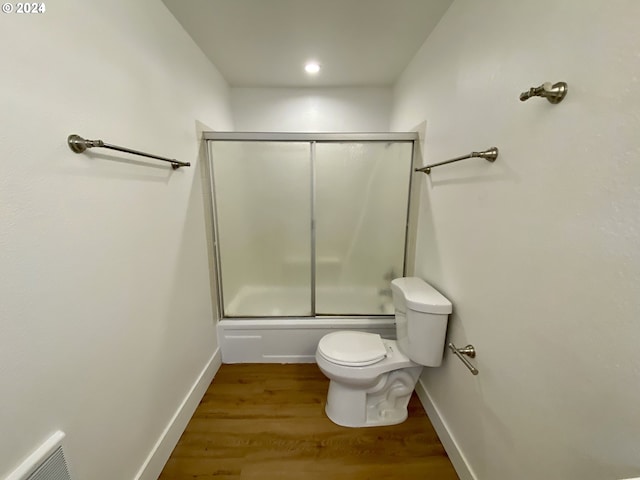 bathroom featuring wood-type flooring, shower / bath combination with glass door, and toilet