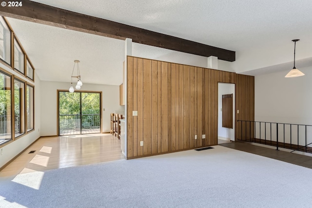 empty room featuring wood-type flooring, vaulted ceiling with beams, a textured ceiling, and wood walls