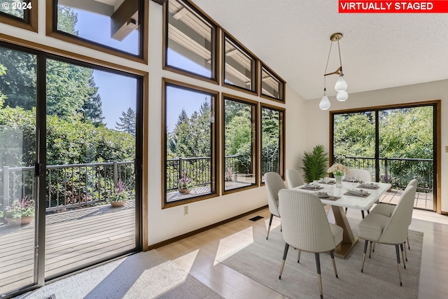 dining area featuring high vaulted ceiling, light hardwood / wood-style floors, and a textured ceiling