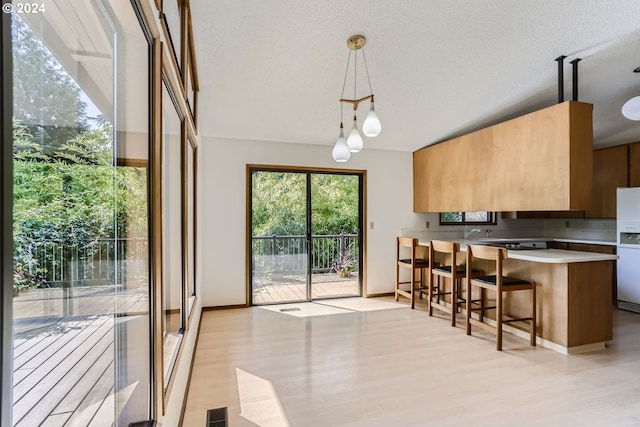 kitchen with light hardwood / wood-style floors, a breakfast bar, kitchen peninsula, pendant lighting, and white fridge with ice dispenser