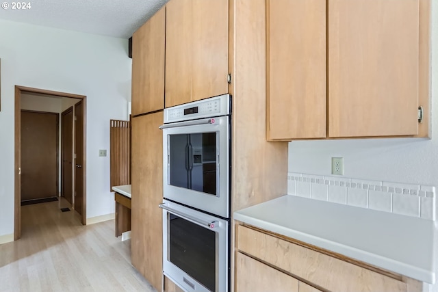 kitchen featuring a textured ceiling, double oven, light brown cabinets, and light hardwood / wood-style flooring