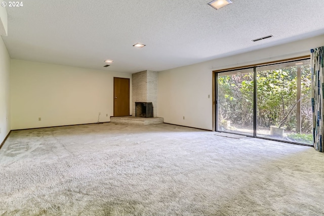 unfurnished living room featuring a brick fireplace, a textured ceiling, and light colored carpet