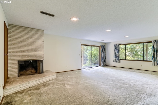 unfurnished living room featuring a brick fireplace, a textured ceiling, and carpet flooring