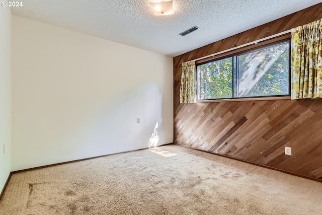 spare room featuring wood walls, a textured ceiling, and carpet floors