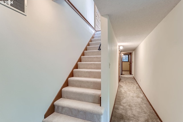 stairs with carpet floors and a textured ceiling