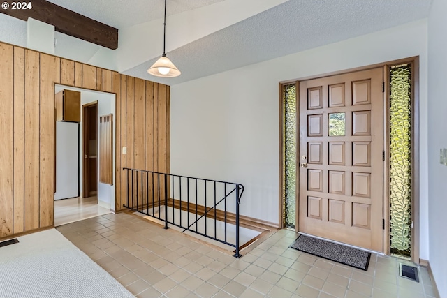 entrance foyer with a textured ceiling, wooden walls, lofted ceiling with beams, and light tile patterned floors