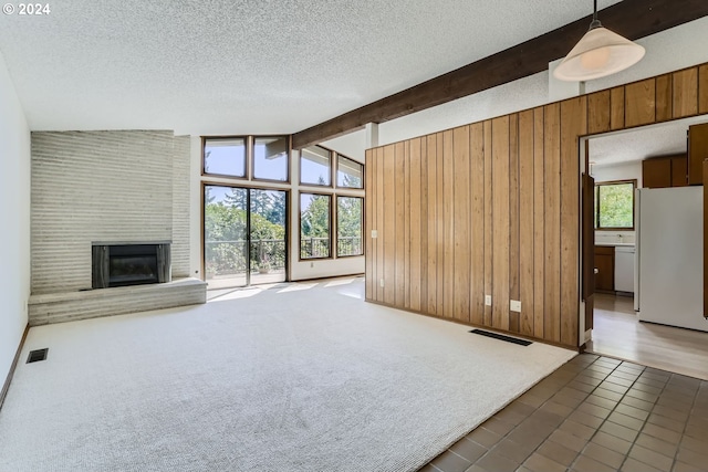 unfurnished living room featuring a textured ceiling, vaulted ceiling with beams, dark carpet, and a brick fireplace