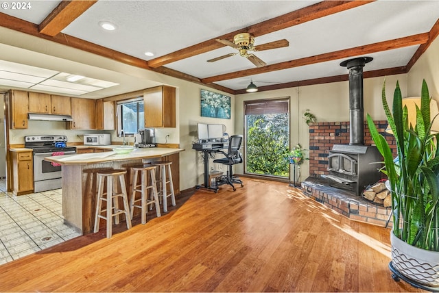 kitchen with a wood stove, electric range, a kitchen breakfast bar, light hardwood / wood-style flooring, and kitchen peninsula