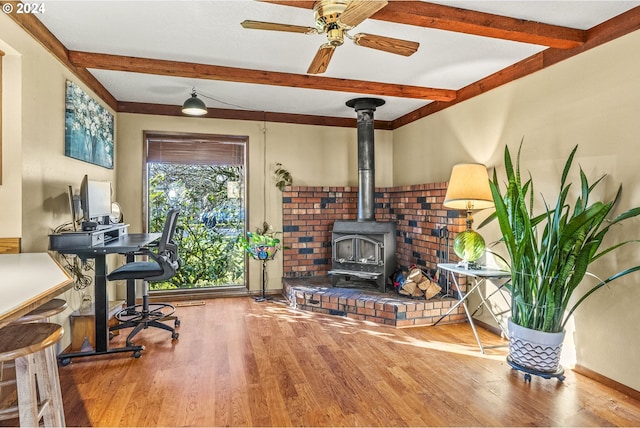 office featuring beamed ceiling, ceiling fan, a wood stove, and hardwood / wood-style floors