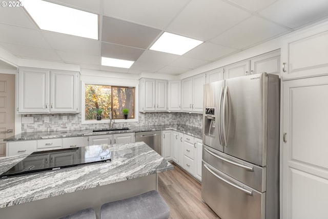 kitchen with sink, white cabinetry, backsplash, stainless steel appliances, and light stone countertops