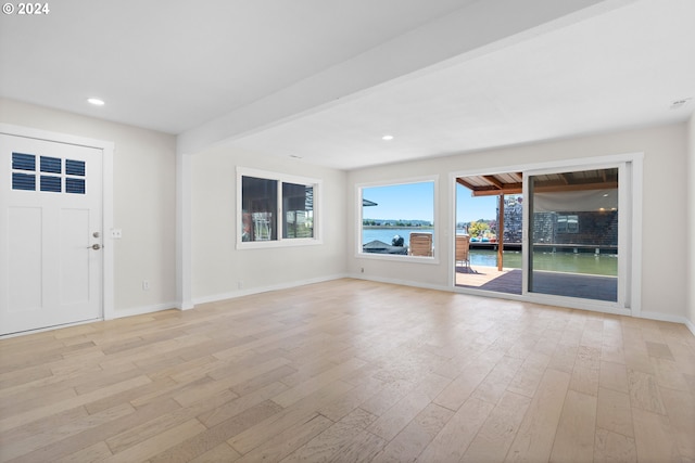 unfurnished living room featuring light wood-type flooring, beam ceiling, and a water view