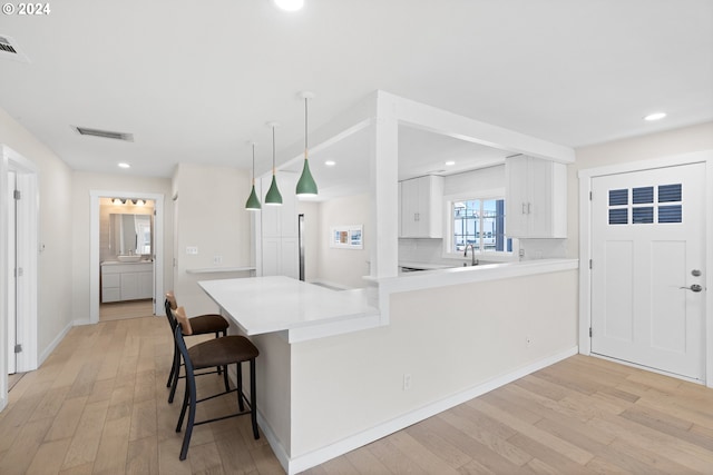 kitchen featuring light wood-type flooring, backsplash, decorative light fixtures, and white cabinets