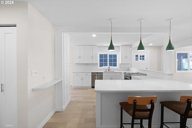 kitchen with light hardwood / wood-style flooring, white cabinets, kitchen peninsula, appliances with stainless steel finishes, and a breakfast bar area