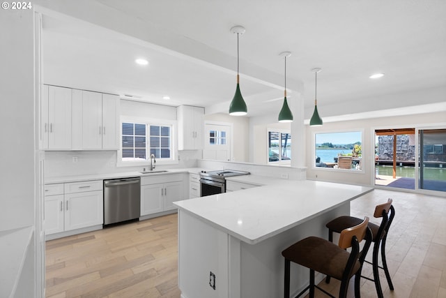 kitchen featuring stainless steel appliances, light hardwood / wood-style flooring, a kitchen bar, white cabinets, and hanging light fixtures