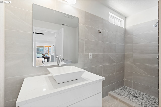 bathroom featuring a tile shower, vanity, and tile walls