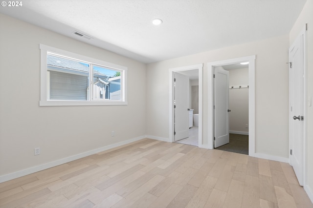 unfurnished bedroom with a spacious closet, a closet, light hardwood / wood-style floors, and connected bathroom