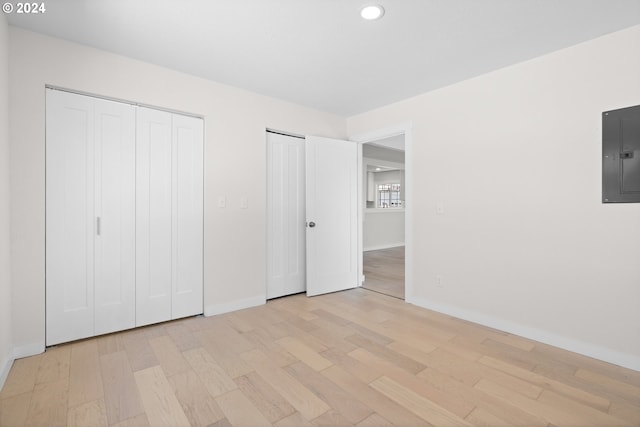 unfurnished bedroom featuring light hardwood / wood-style flooring, electric panel, and two closets