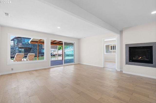 unfurnished living room with light hardwood / wood-style floors, plenty of natural light, and beamed ceiling