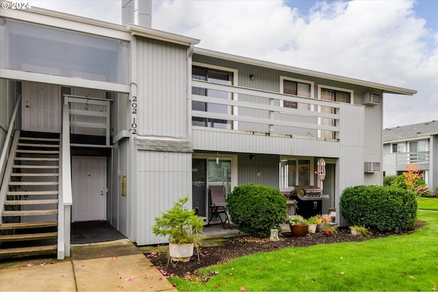 rear view of property featuring a yard, a wall mounted air conditioner, and a balcony