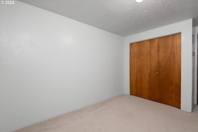 unfurnished bedroom featuring light colored carpet, a textured ceiling, and a closet