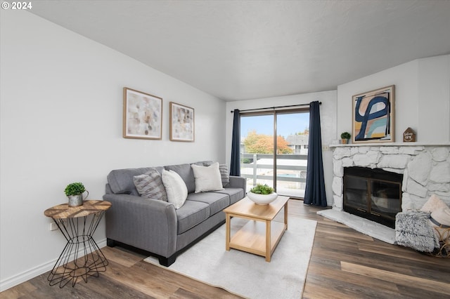 living room featuring a stone fireplace and dark hardwood / wood-style flooring