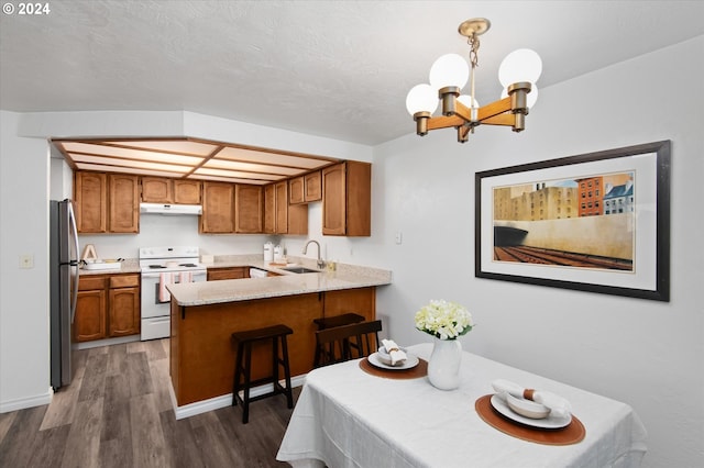 kitchen featuring white electric range oven, kitchen peninsula, sink, stainless steel refrigerator, and pendant lighting