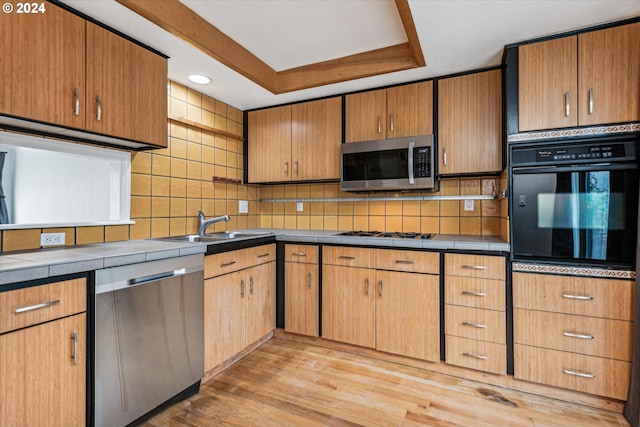 kitchen featuring a raised ceiling, sink, light hardwood / wood-style flooring, tasteful backsplash, and stainless steel appliances