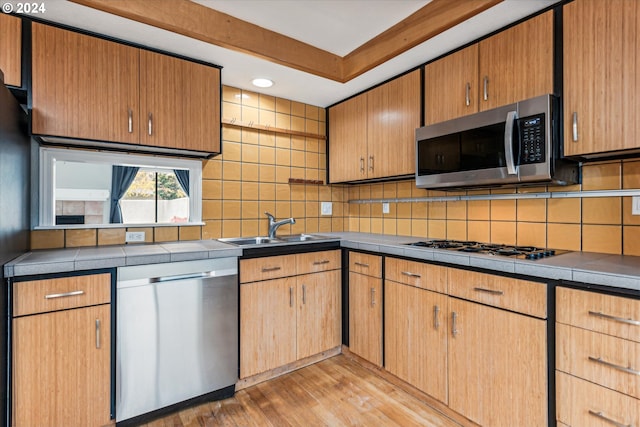 kitchen with tasteful backsplash, sink, light hardwood / wood-style flooring, and appliances with stainless steel finishes