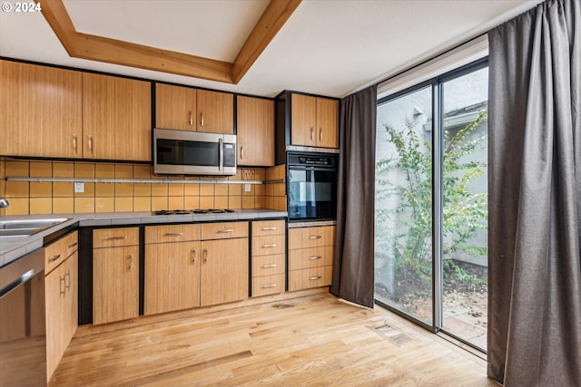 kitchen with sink, light hardwood / wood-style flooring, backsplash, a tray ceiling, and appliances with stainless steel finishes