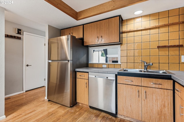 kitchen with decorative backsplash, appliances with stainless steel finishes, sink, light hardwood / wood-style flooring, and tile counters