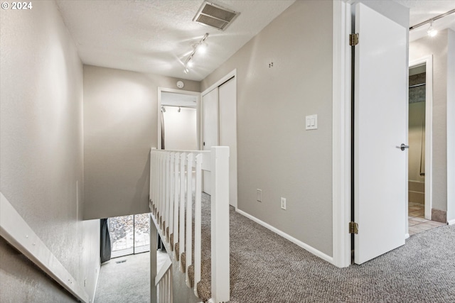 hallway with a textured ceiling, light colored carpet, and track lighting