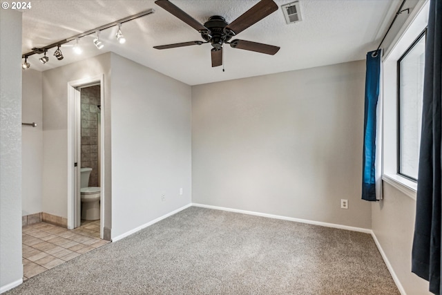 unfurnished bedroom with light carpet, rail lighting, ensuite bath, ceiling fan, and a textured ceiling