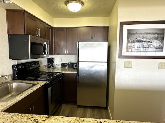 kitchen with light stone countertops, dark hardwood / wood-style flooring, appliances with stainless steel finishes, dark brown cabinets, and sink